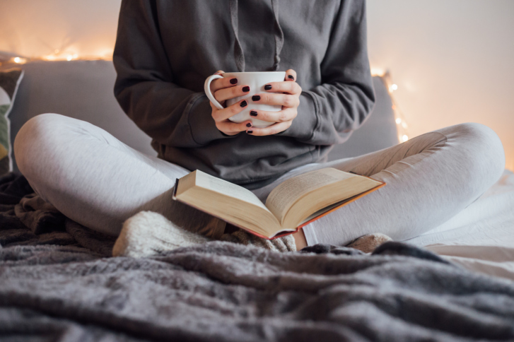 Girl drinking hot tea and reading book in bed